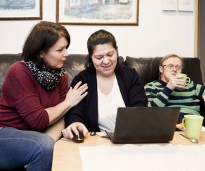 Healthcare worker helping woman with down syndrome in using laptop while man having drink at sofa Healthcare worker helping woman with down syndrome in using laptop while man having drink at sofa